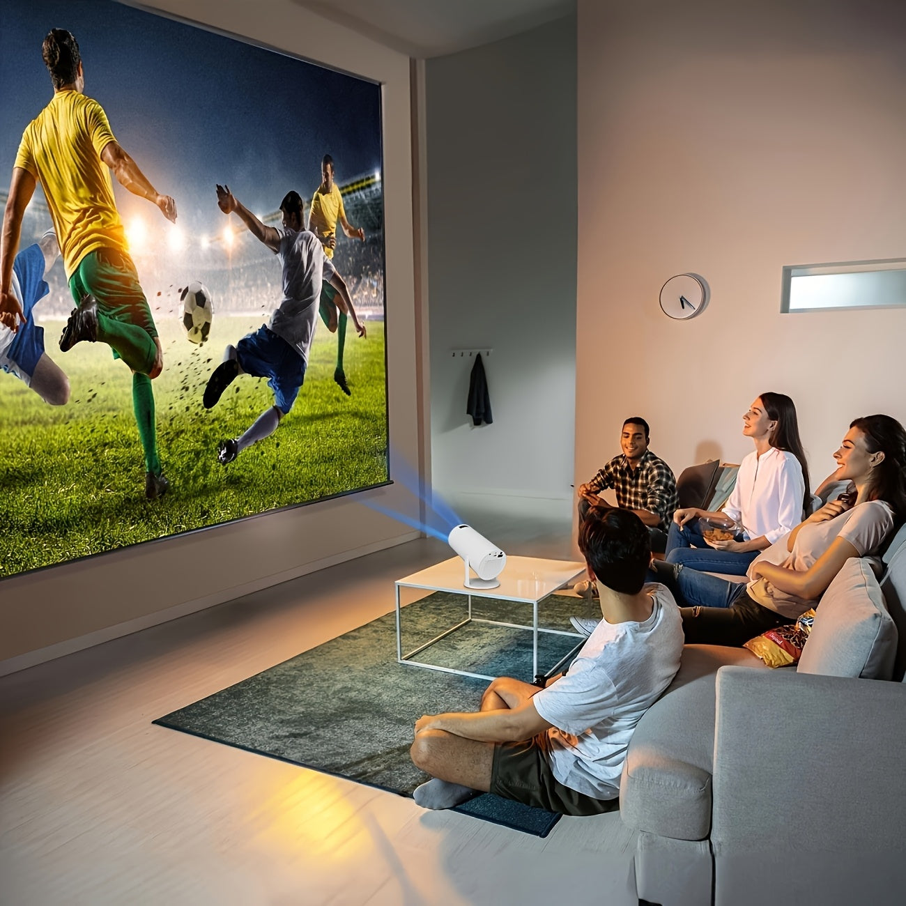 Full HD 1080p mini projector displaying a soccer match on a large screen, with viewers seated on a couch.